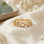 Photographie de produit d'une bague à maillons gourmette dorés entièrement pavée de cristaux, fond neutre.