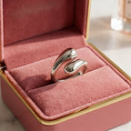 Bague argentée Alya Audacieuse présentée dans un luxueux écrin de velours rose. Bijou de créateur aux courbes fluides et brillantes.