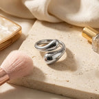 Mise en scène lifestyle de la bague argentée Alya Audacieuse sur un socle en pierre naturelle avec accessoires de beauté en arrière-plan.