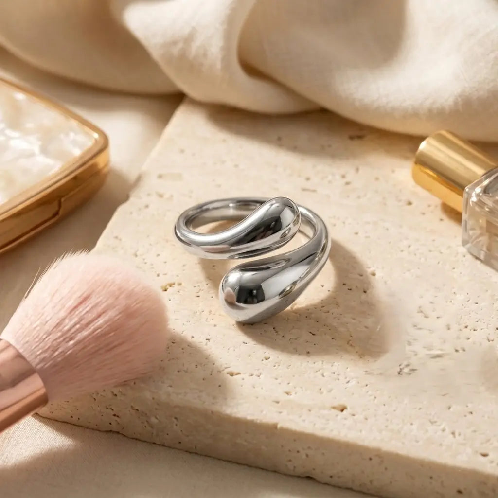 Mise en scène lifestyle de la bague argentée Alya Audacieuse sur un socle en pierre naturelle avec accessoires de beauté en arrière-plan.