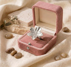 Bague argentée en forme de fleur posée dans un écrin en velours rose poudré, style poétique et délicat.