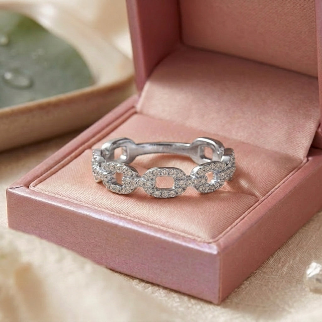 Gros plan d'une bague anneau gourmette argentée sertie de zircons brillants dans un écrin rose ouvert.