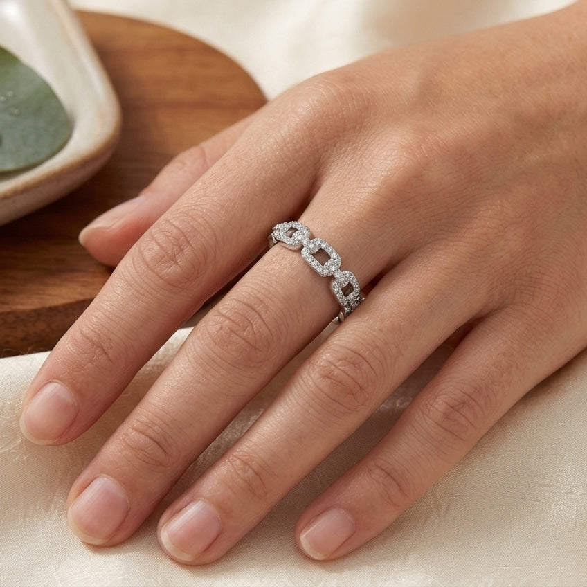 Bague maille gourmette argentée en acier inoxydable pavée de zircons, portée à la main d'une femme.