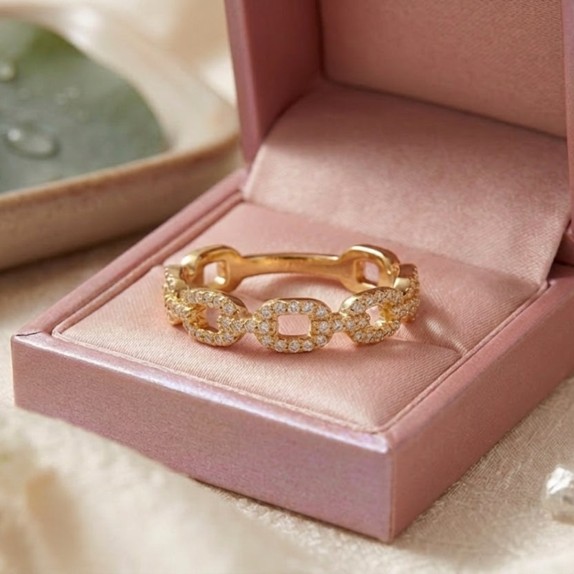 Gros plan d'une bague anneau gourmette dorée sertie de zircons brillants dans un écrin rose ouvert.