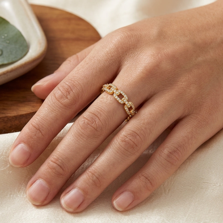 Bague maille gourmette dorée en acier inoxydable pavée de zircons, portée à la main d'une femme.
