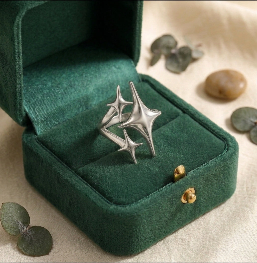 Bague triple étoile argentée Cassiopée Filante présentée dans un écrin velours vert ouvert.