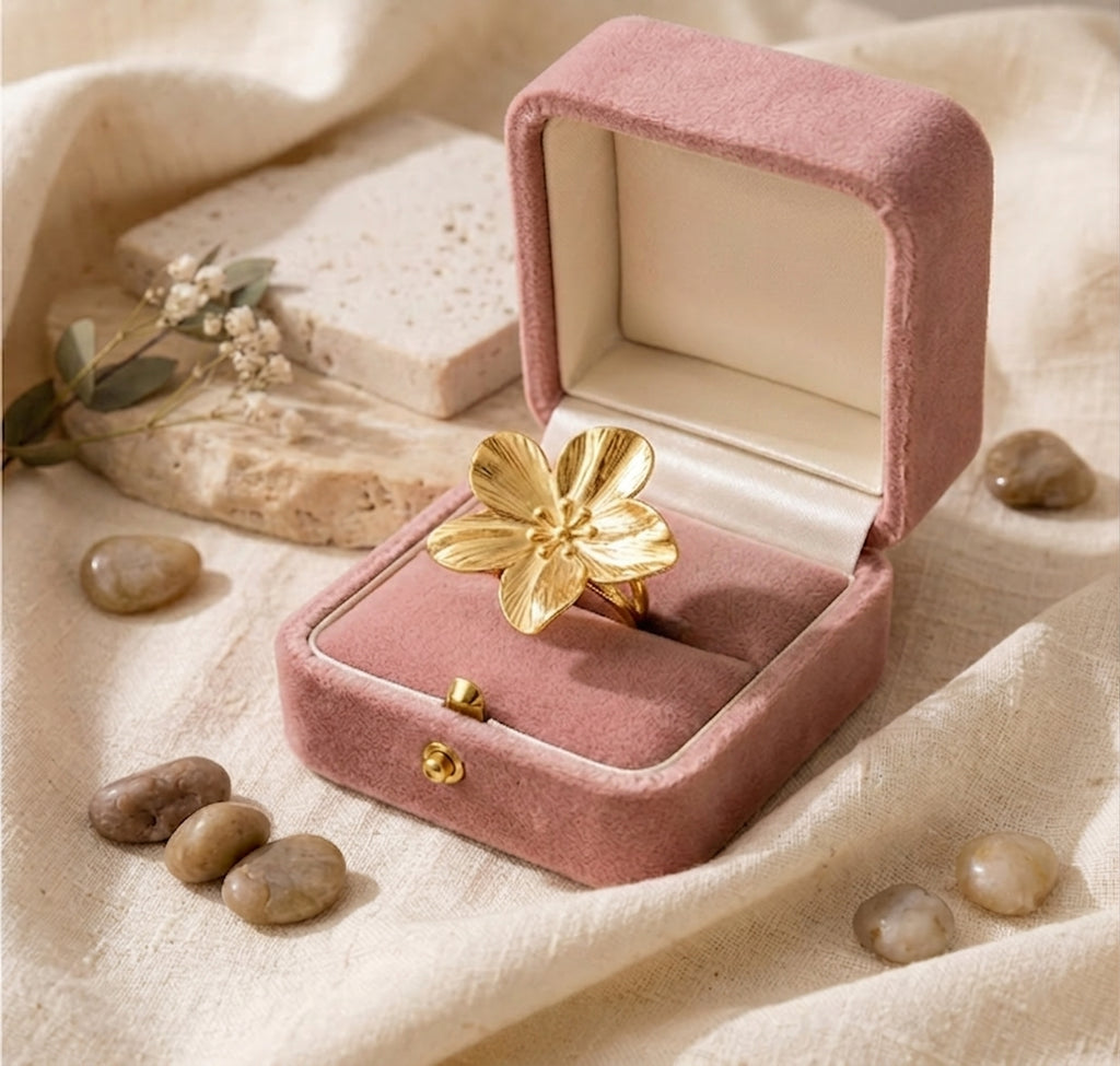 Bague dorée en forme de fleur posée dans un écrin en velours rose poudré, style poétique et délicat.