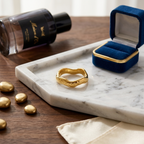 Bijou bague Zoé dorée posée sur un plateau en marbre à côté d'un écrin en velours bleu roi.