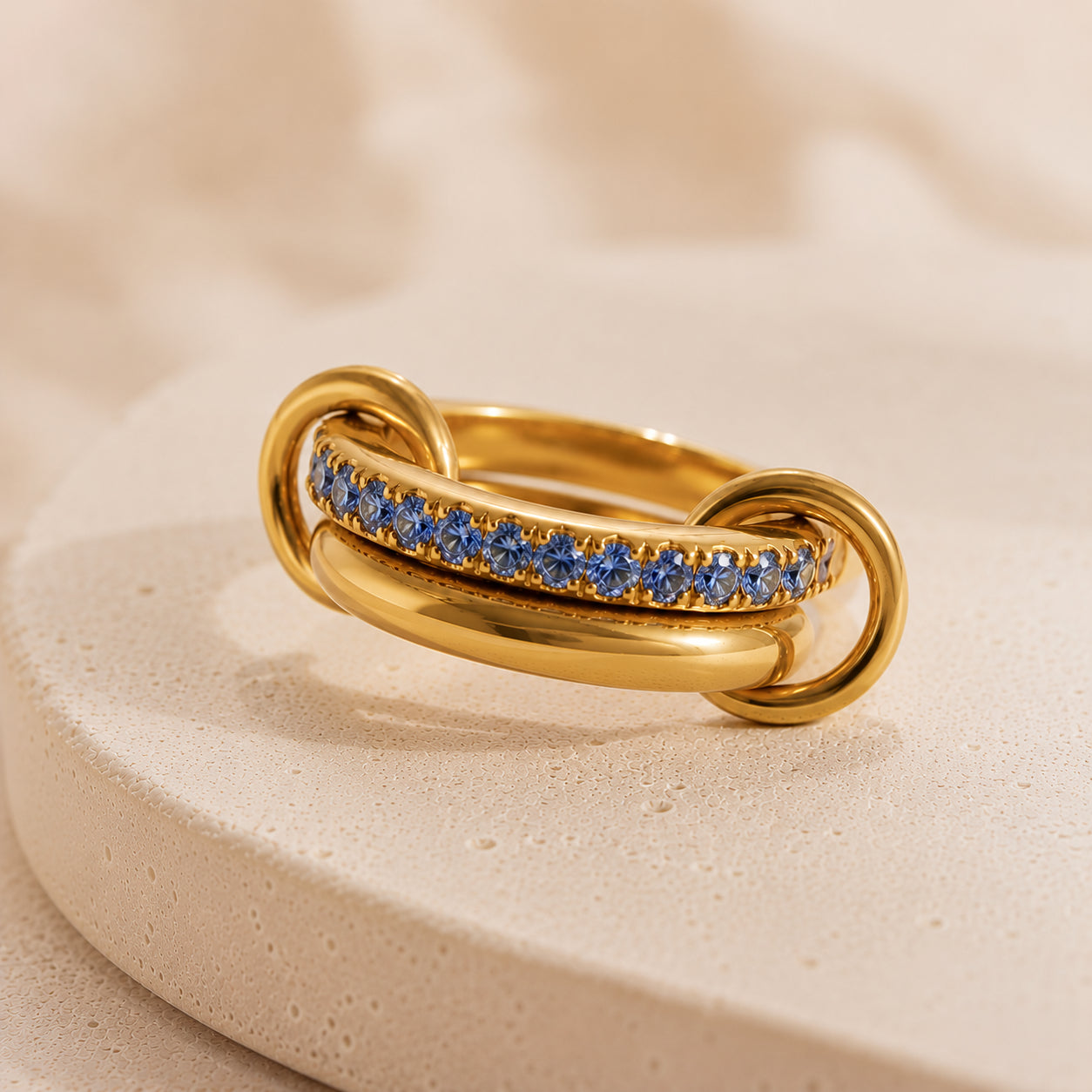 Bague Entrelacée Harmonie en acier inoxydable doré avec pierres bleues sur fond beige