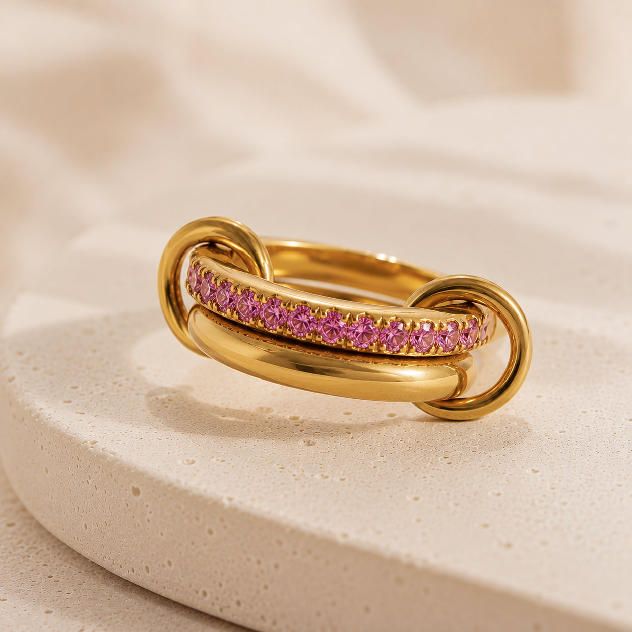 Bague Entrelacée Harmonie en acier inoxydable doré avec pierres roses sur fond beige