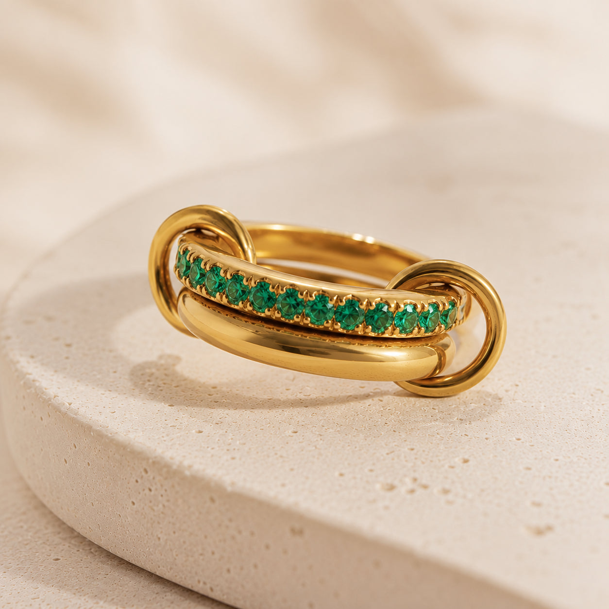 Bague Entrelacée Harmonie en acier inoxydable doré avec pierres vertes sur fond beige