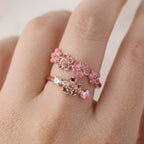 Gros plan sur une bague fleur de pêcher dorée portée sur un doigt, montrant les détails floraux rosés.