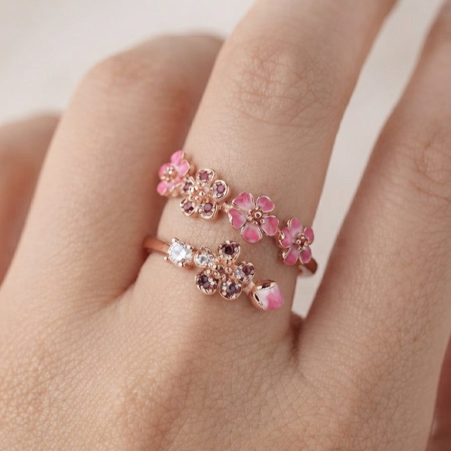 Gros plan sur une bague fleur de pêcher dorée portée sur un doigt, montrant les détails floraux rosés.
