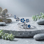 Bague fleur de pêcher argentée mise en scène sur un support minéral gris, design printanier.