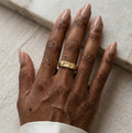 Gros plan d'une main avec la bague Gabrielle Indomptable dorée texturé, design brut.