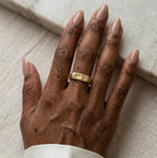 Gros plan d'une main avec la bague Gabrielle Indomptable dorée texturé, design brut.
