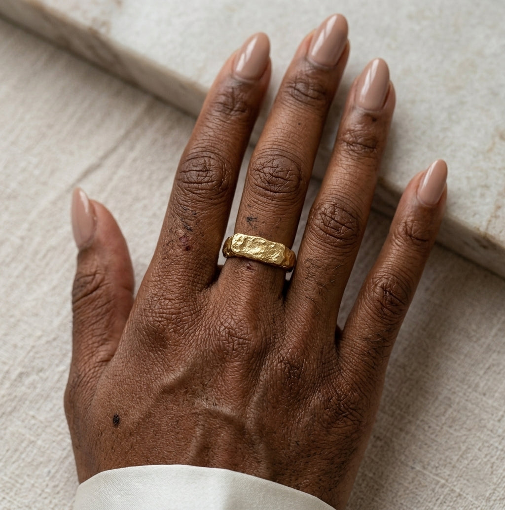 Gros plan d'une main avec la bague Gabrielle Indomptable dorée texturé, design brut.