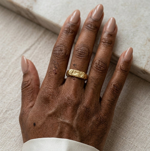 Gros plan d'une main avec la bague Gabrielle Indomptable dorée texturé, design brut.