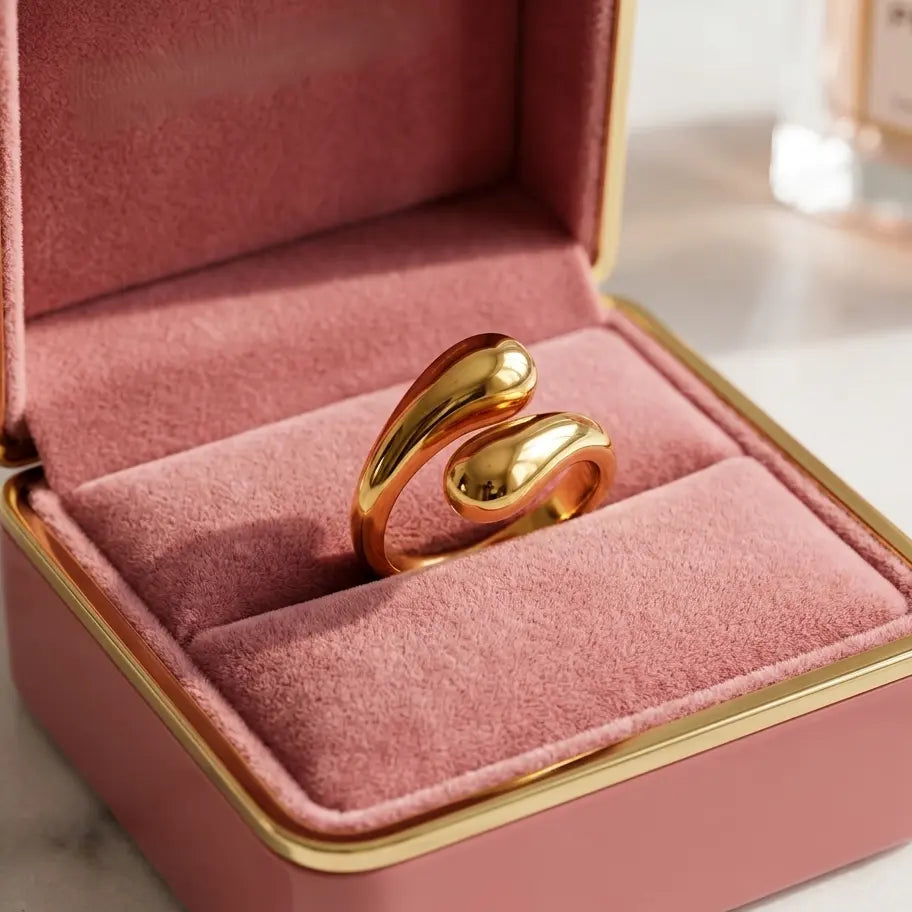 Bague dorée Alya Audacieuse présentée dans un luxueux écrin de velours rose. Bijou de créateur aux courbes fluides et brillantes.