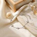Bracelet multi-trèfles argenté Margaux Fine mis en scène dans un décor chic. Le bijou scintille sur un support minéral texturé, contrastant avec la douceur d'un tissu satiné crème et des pétales de fleurs séchées baignés dans une lumière solaire douce.