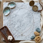 Bijou de corps Zora Nomade en finition argentée disposé à plat sur un plateau en marbre avec des accessoires marins et lavande.