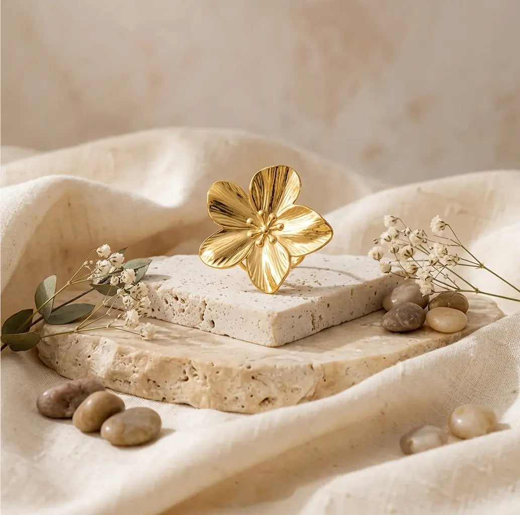Bague dorée en forme de pétale présentée sur une pierre naturelle et un tissu en lin beige, ambiance douce et épurée.