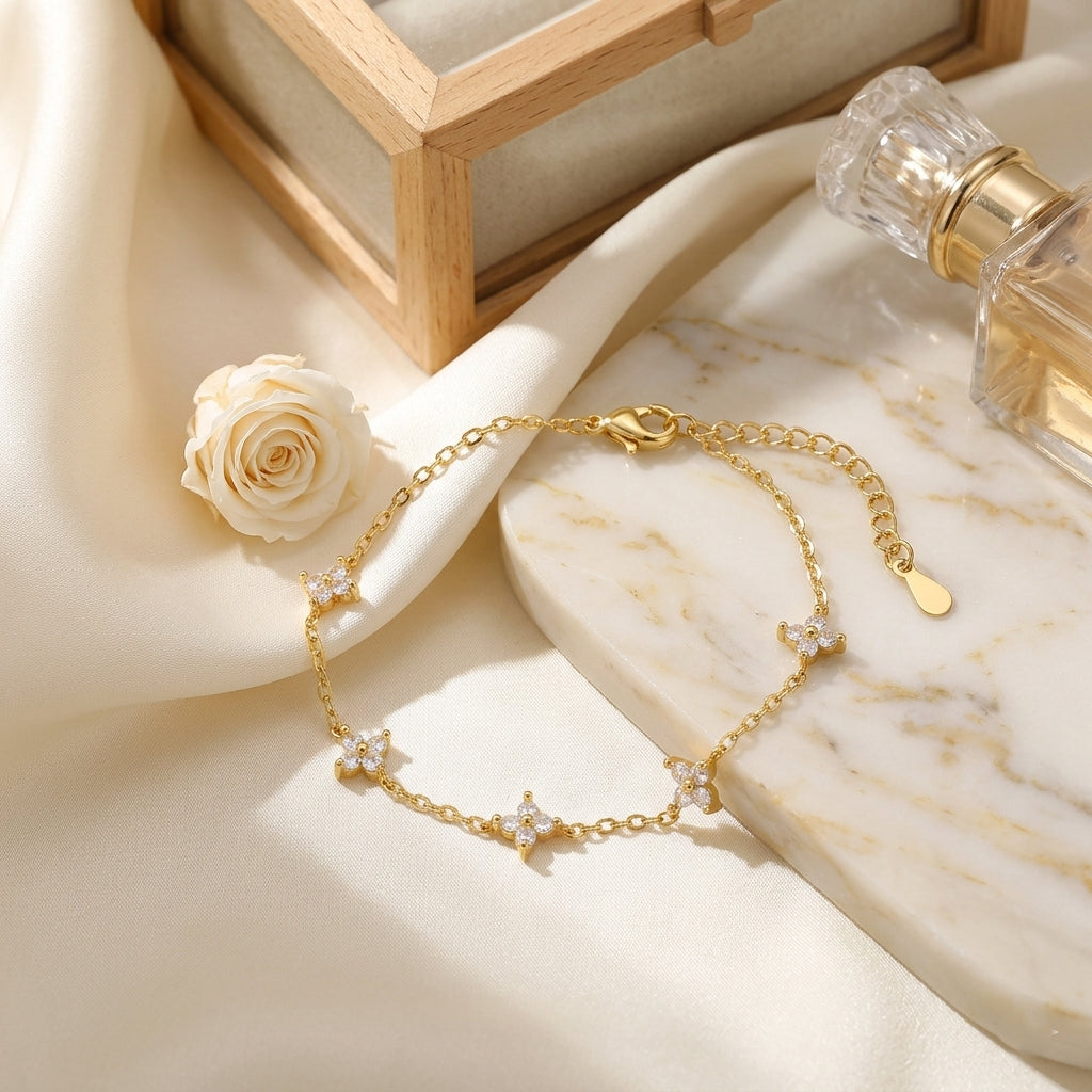 Composition luxueuse présentant le bracelet doré Margaux Fine déposé sur une plaque de marbre blanc veiné. Le bijou est entouré d'un drapé de soie ivoire fluide, d'un flacon de parfum en cristal et d'une rose blanche, créant une atmosphère de vanité moderne et élégante.