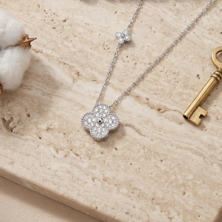 Zoom sur le pendentif trèfle argenté du collier Livia Radieuse posé sur un socle en marbre, avec une clé dorée ancienne en décoration.