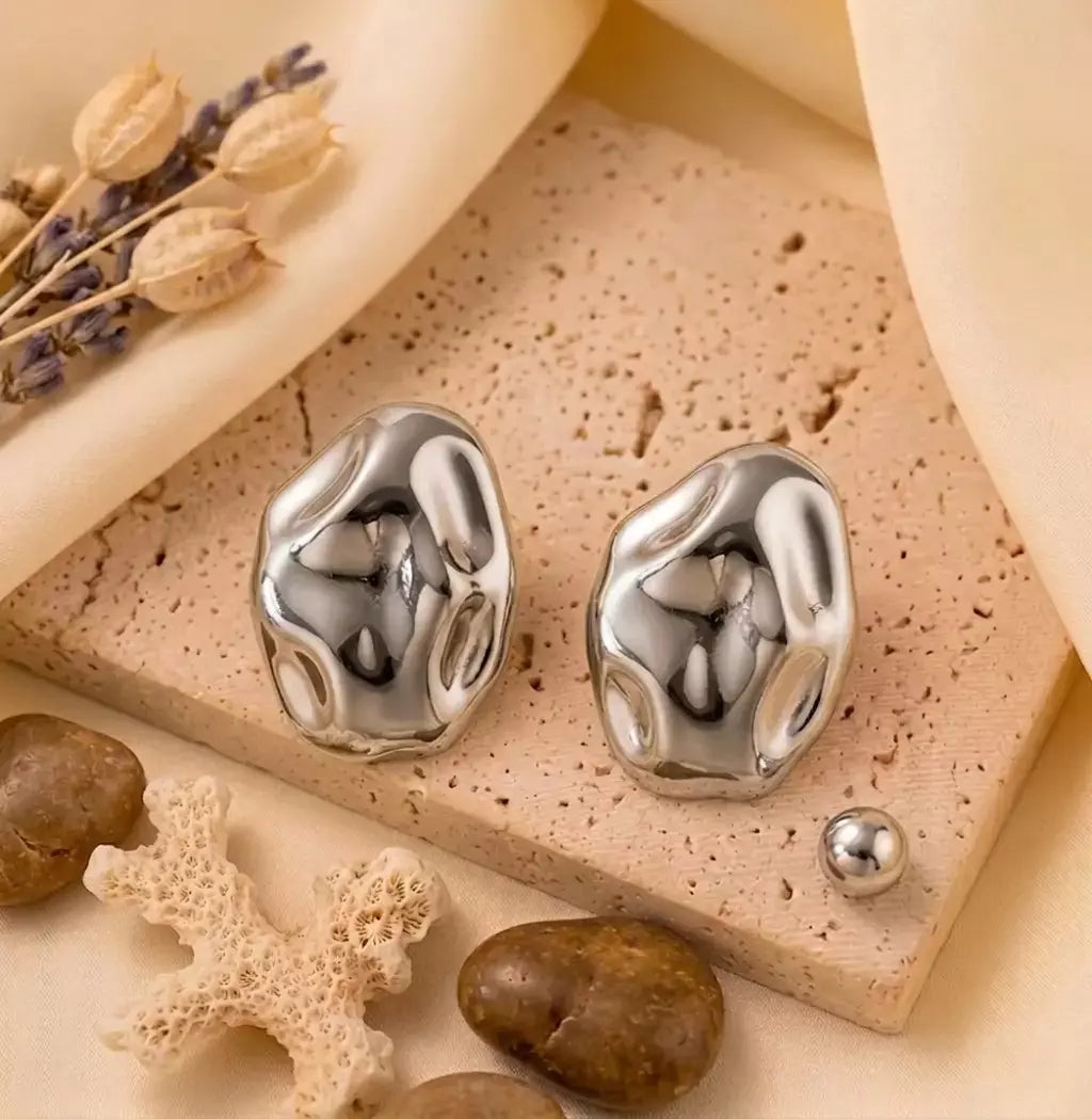 Paire de boucles d'oreilles argentées Léna - Aquatique posée sur un support en pierre beige, soulignant leur forme fluide et leur éclat solaire.