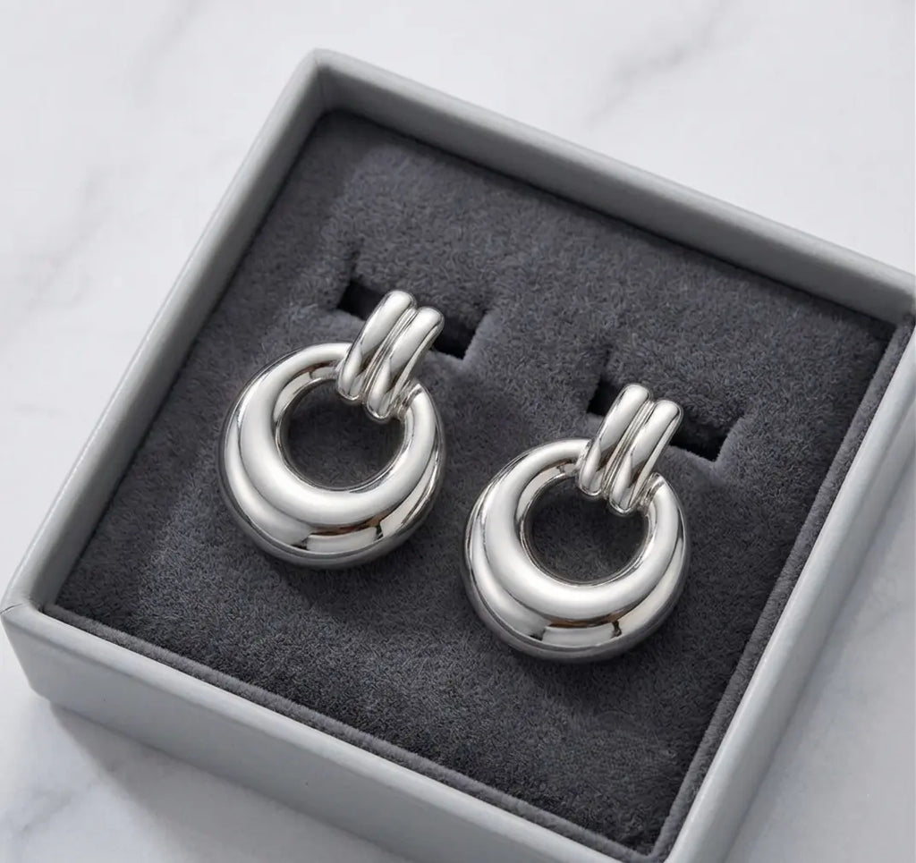 Paire de boucles d'oreilles argentées Alba présentée dans un écrin de luxe minimaliste gris avec un intérieur en velours anthracite, posé sur du marbre.