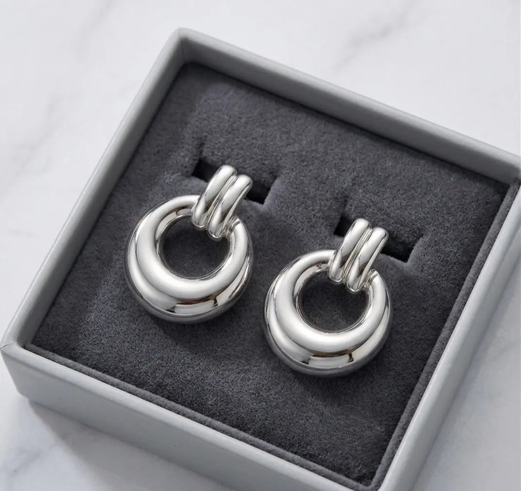 Paire de boucles d'oreilles argentées Alba présentée dans un écrin de luxe minimaliste gris avec un intérieur en velours anthracite, posé sur du marbre.
