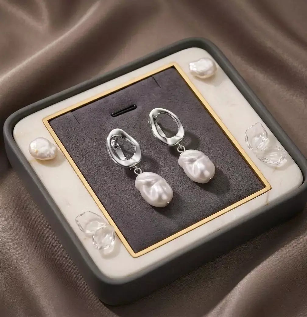 Vue du dessus des boucles d'oreilles Clarisse - Nacrée en argent précieuse présentées dans leur écrin haut de gamme en velours gris. Le cadeau idéal au design singulier.