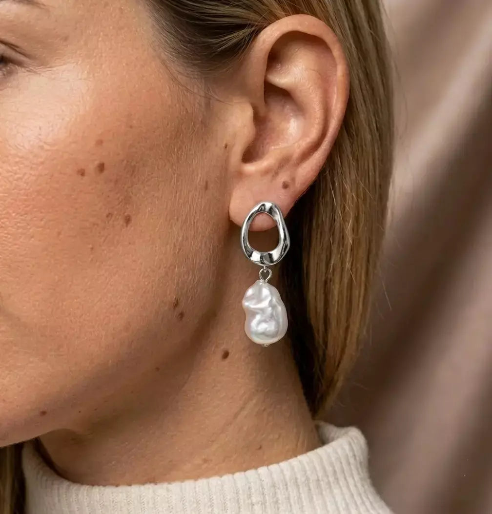 Plan rapproché d'un mannequin de profil portant la boucle d'oreille Clarisse - Nacrée en argent précieux. L'anneau torsadé argent et la perle baroque nacrée scintillent doucement.