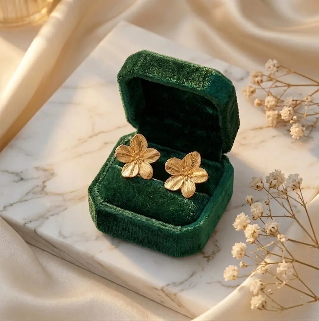 Boucles d'oreilles Léonie Majestueuse doré présentées dans un écrin de luxe en velours vert émeraude. Le coffret est posé sur du marbre, accompagné de fleurs de gypsophile séchées pour une ambiance romantique.