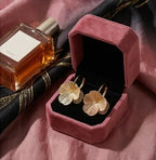 une paire de boucles d'oreilles Eléonore en acier inoxydable doré brossé et texturé, présentées dans un écrin de luxe en velours vieux rose ouvert.