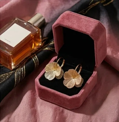 une paire de boucles d'oreilles Eléonore en acier inoxydable doré brossé et texturé, présentées dans un écrin de luxe en velours vieux rose ouvert.