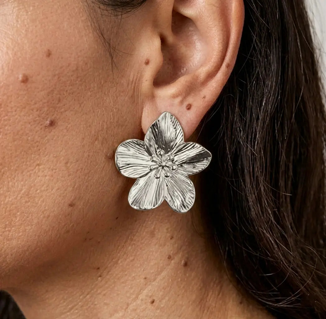 Gros plan sur le profil d'une femme portant une boucle d'oreille "Léonie Majestueuse" en argent. Le bijou, en forme de fleur épanouie aux pétales finement texturés et striés, apporte une touche d'élégance naturelle.