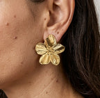 Gros plan sur le profil d'une femme portant une boucle d'oreille "Léonie Majestueuse" doré. Le bijou, en forme de fleur épanouie aux pétales finement texturés et striés, apporte une touche d'élégance naturelle.