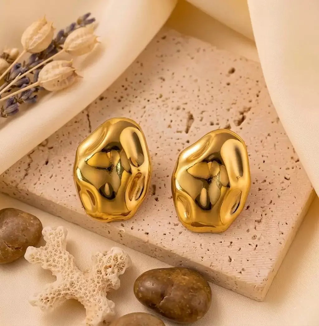 Paire de boucles d'oreilles dorées Léna - Aquatique posée sur un support en pierre beige, soulignant leur forme fluide et leur éclat solaire.