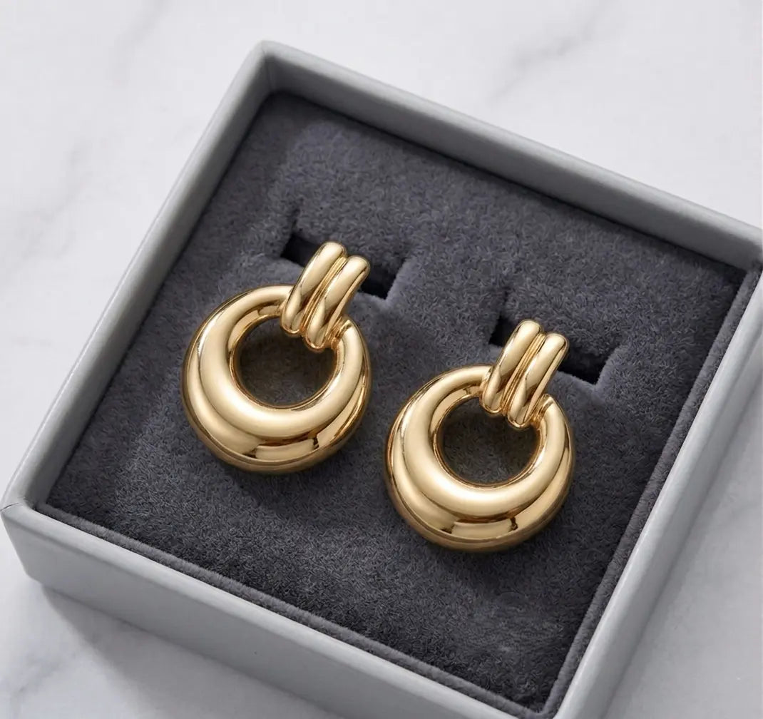 Paire de boucles d'oreilles dorées Alba présentée dans un écrin de luxe minimaliste gris avec un intérieur en velours anthracite, posé sur du marbre.
