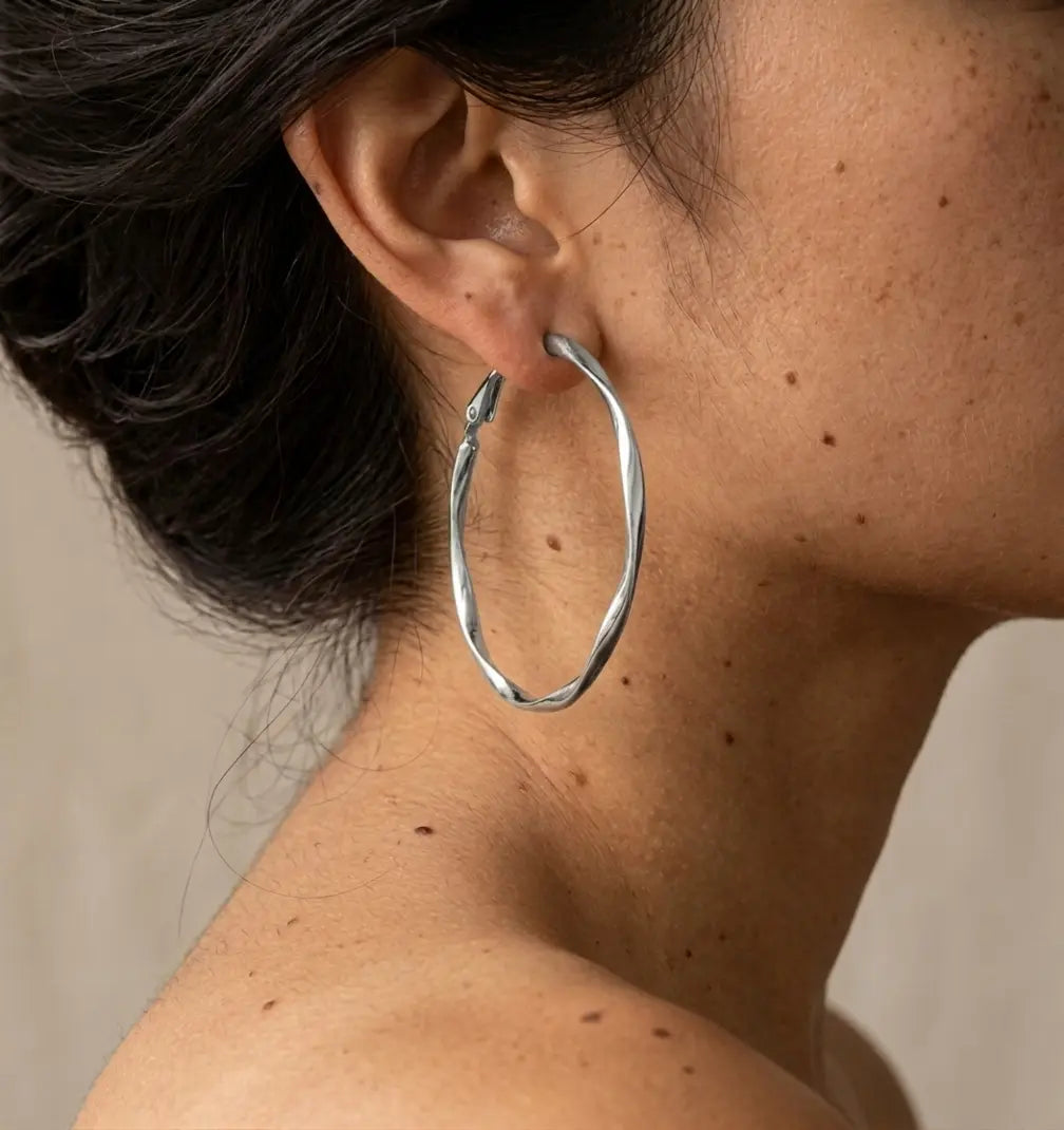 Gros plan réaliste d'une boucle d'oreille argentée Élise Élégante portée par une mannequin. On distingue les détails de la peau et le mouvement torsadé du bijou argenté qui apporte un éclat sophistiqué.
