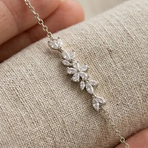 Gros plan détaillé sur le motif central floral en oxydes de zirconium taille marquise du bracelet argenté Chloé de Maison Dosana, suspendu au-dessus d'un tissu en lin texturé. L'acier inoxydable argenté et les zircons brillent sous la lumière.