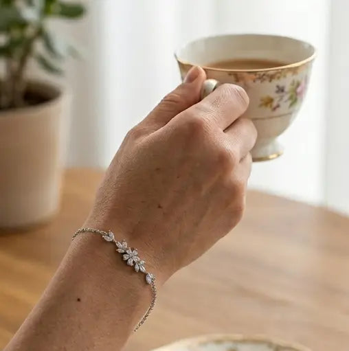 gros plan sur le poignet d'une femme portant la version argentée du bracelet Chloé en acier inoxydable et oxydes de zirconium de Maison Dosana, tenant une tasse de thé vintage. Le bracelet délicat scintille au poignet.