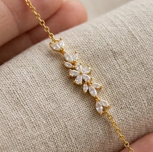 Gros plan détaillé sur le motif central floral en oxydes de zirconium taille marquise du bracelet Chloé de Maison Dosana, suspendu au-dessus d'un tissu en lin texturé. L'acier inoxydable doré et les zircons brillent sous la lumière.