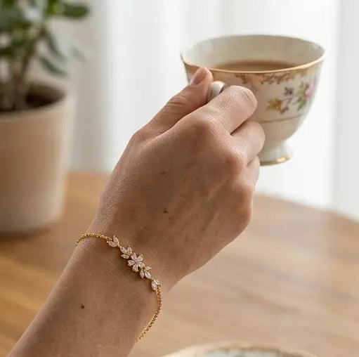 gros plan sur le poignet d'une femme portant le bracelet Chloé en acier inoxydable doré et oxydes de zirconium de Maison Dosana, tenant une tasse de thé vintage. Le bracelet délicat scintille au poignet.