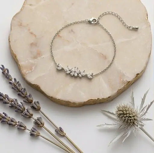 Vue d'ensemble à plat du bracelet argenté Chloé - Étincelante de Maison Dosana reposant sur une plaque de marbre rose avec des fleurs séchées. Le bracelet en acier inoxydable argenté présente un motif floral central en zircons brillants.