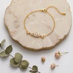 Vue d'ensemble à plat du bracelet Chloé - Étincelante de Maison Dosana reposant sur une plaque de marbre rose avec des fleurs séchées. Le bracelet en acier inoxydable doré présente un motif floral central en zircons brillants.