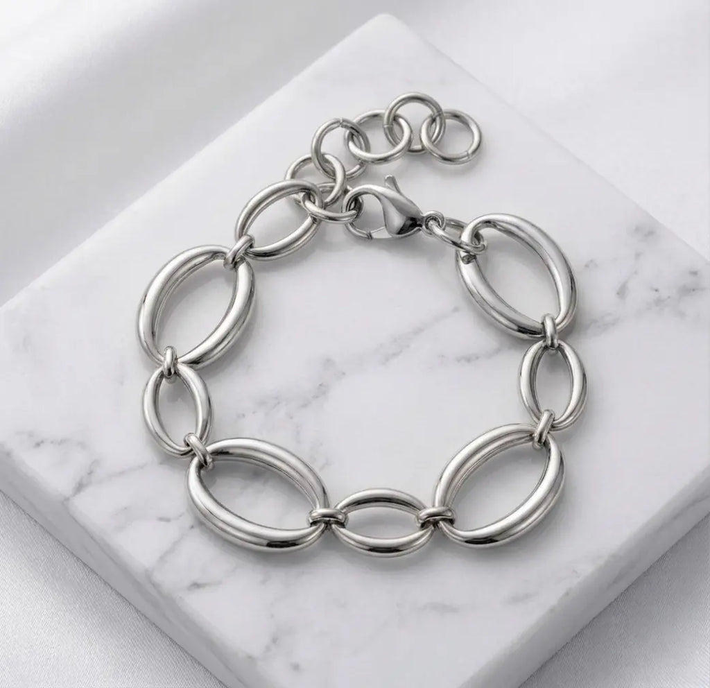 Photographie à plat (flat lay) du bracelet argenté Victoire Vibrante. Il est posé sur un bloc de marbre blanc veiné, sur un fond de satin blanc. Les maillons ovales et le fermoir mousqueton sont bien visibles.