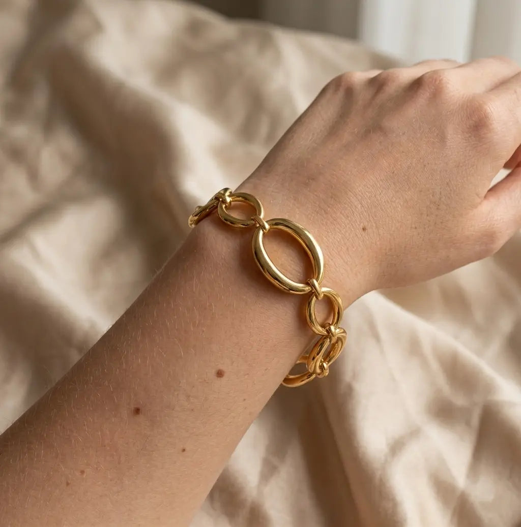 Gros plan réaliste sur le bracelet doré Victoire Vibrante, composé de maillons ovales et ronds polis, porté au poignet d'un mannequin. Le fond est un tissu beige froissé.