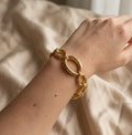 Gros plan réaliste sur le bracelet doré Victoire Vibrante, composé de maillons ovales et ronds polis, porté au poignet d'un mannequin. Le fond est un tissu beige froissé.